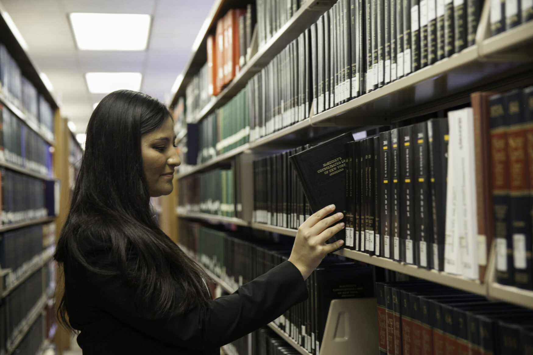 Female student taking a book from a library shelf