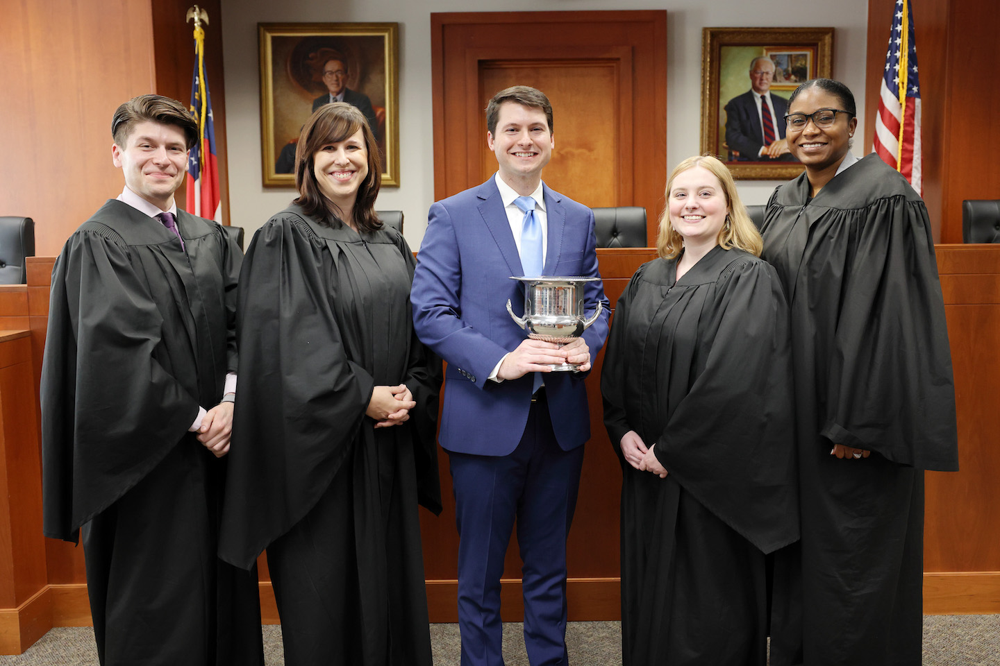 Group of people with judge's robes and a student holding a trophy