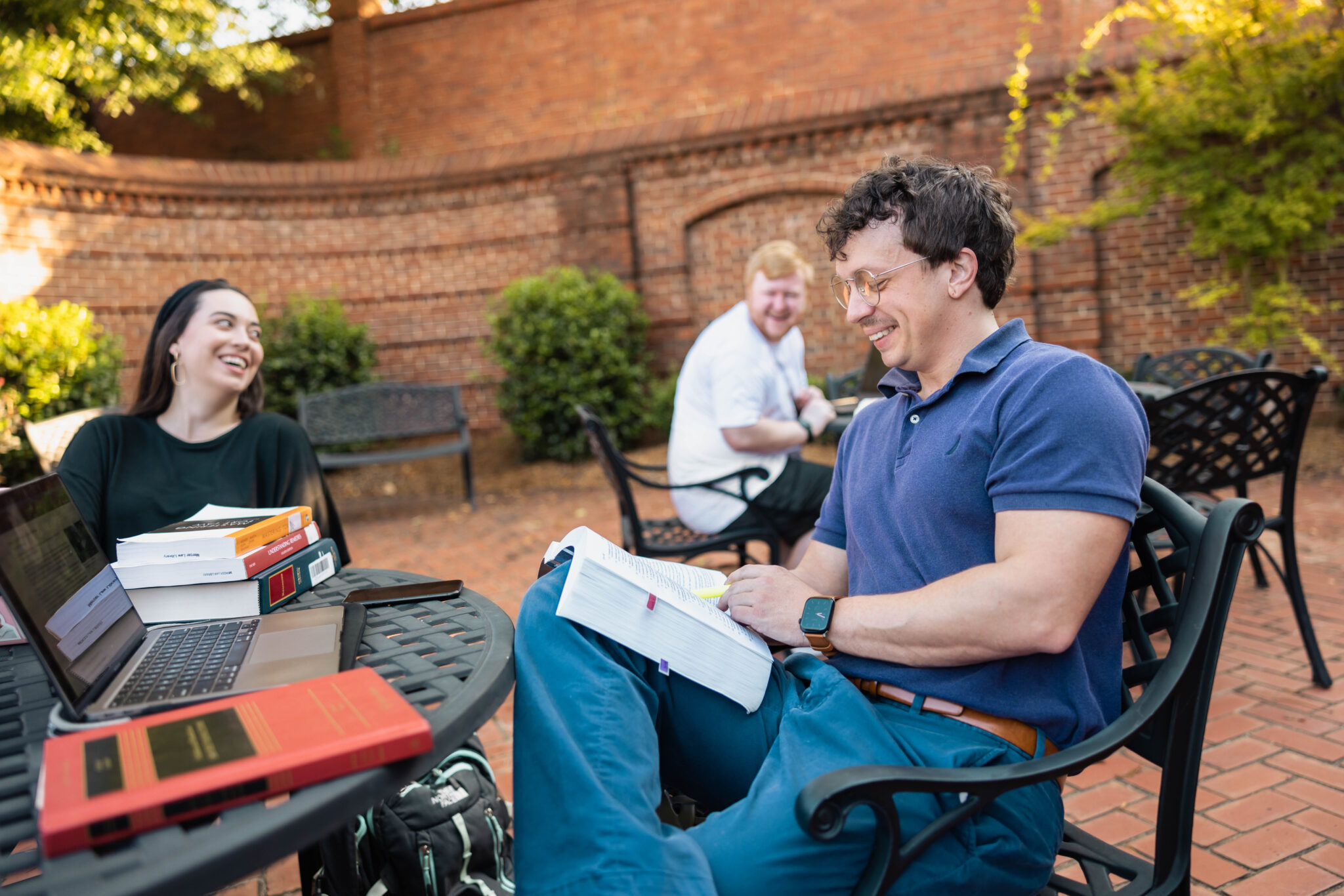 Three students reading books and laughing at an outside table