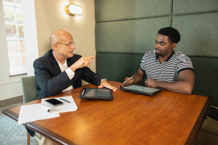 Student and professor talking at a table with laptops