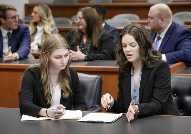 Two students sit behind a table and discuss notes