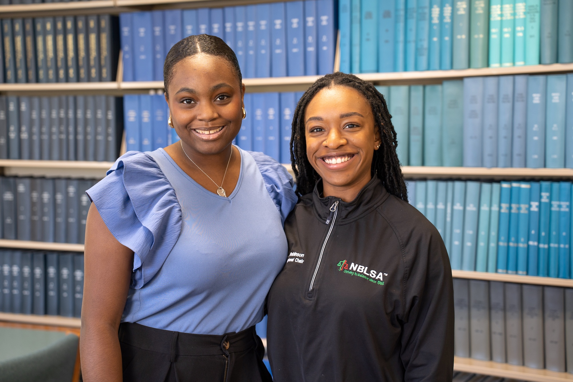 Samantha Archer and Addison Robinson stand in front of a blue wall of books