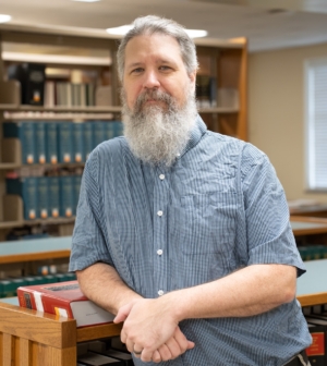 Chris Osier leaning against a bookshelf in the library