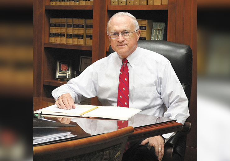 Samuel Ozburn in a white shirt with a red tie sits behind a desk