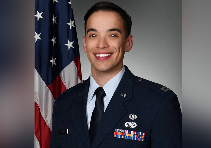 Wesley Watts in a US Air Force uniform stands in front of an American flag