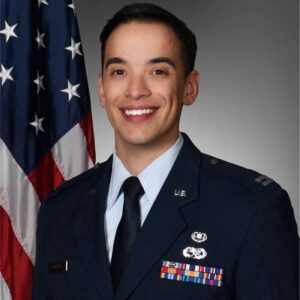 Wesley Watts in a US Air Force uniform stands in front of an American flag