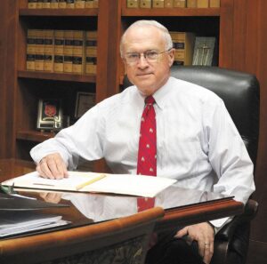 Samuel Ozburn in a white shirt with a red tie sits behind a desk