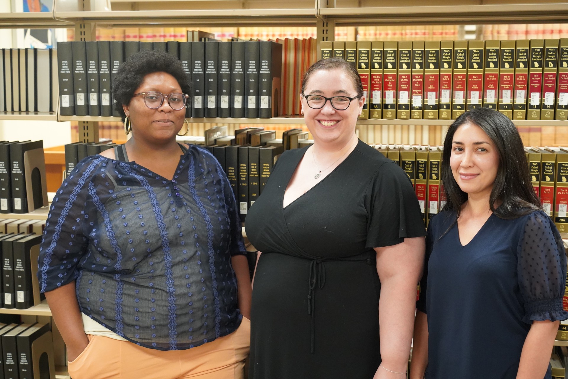 Three female library staff members stand in front of a bookshelf