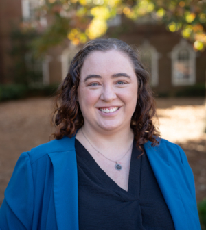 Savanna Nolan in a black shirt and blue jacket standing in front of a tree and brick building