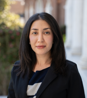 Hamaseh Roozbeh in a black jacket and black and white striped shirt standing on the law school front porch
