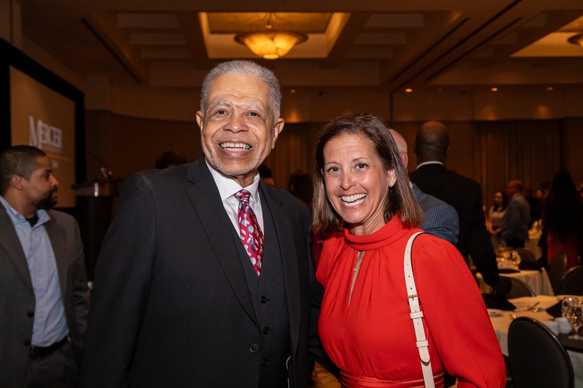 A man in a dark suit stands next to a woman in a red dress