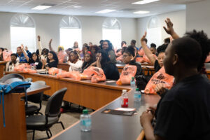 Students sit at tables in a classroom with hands raised