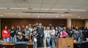 High school students stand in a practice courtroom at Mercer Law School with Judge Story