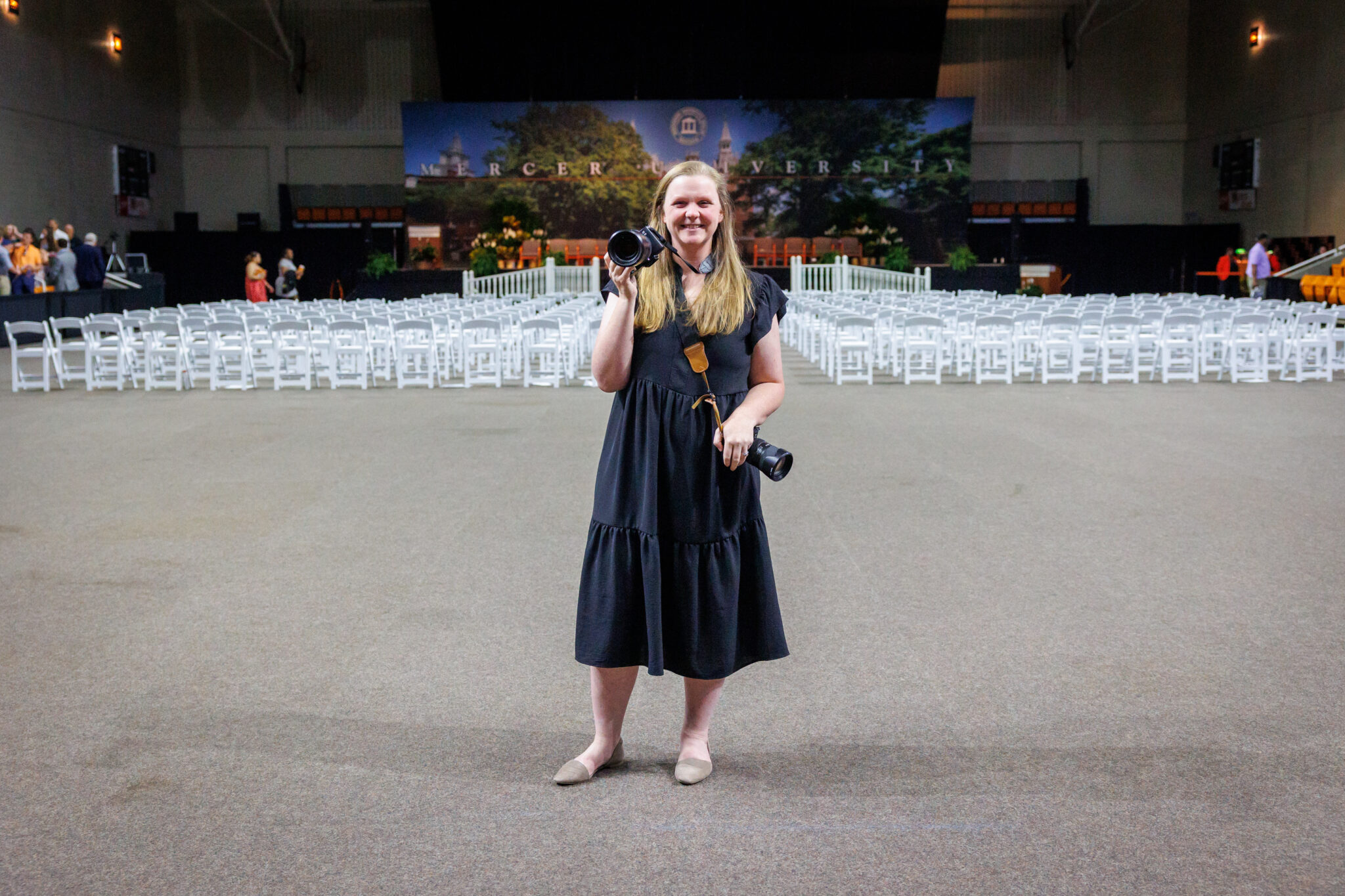 Maggie Reimer stands in Hawkins Arena at graduation, holding two cameras