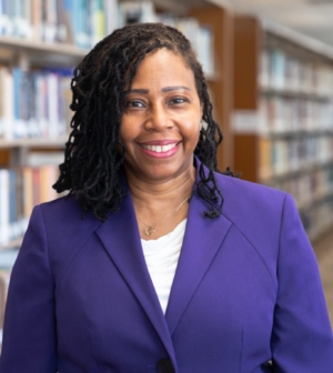 A woman in a purple suit stands in front of library books