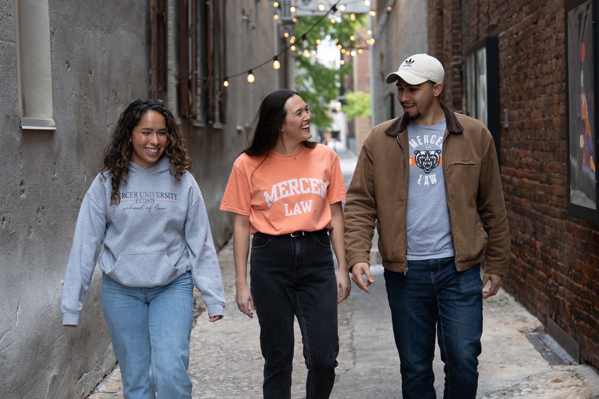 Two female students and one male student in Mercer Law shirts walk down an alleyway