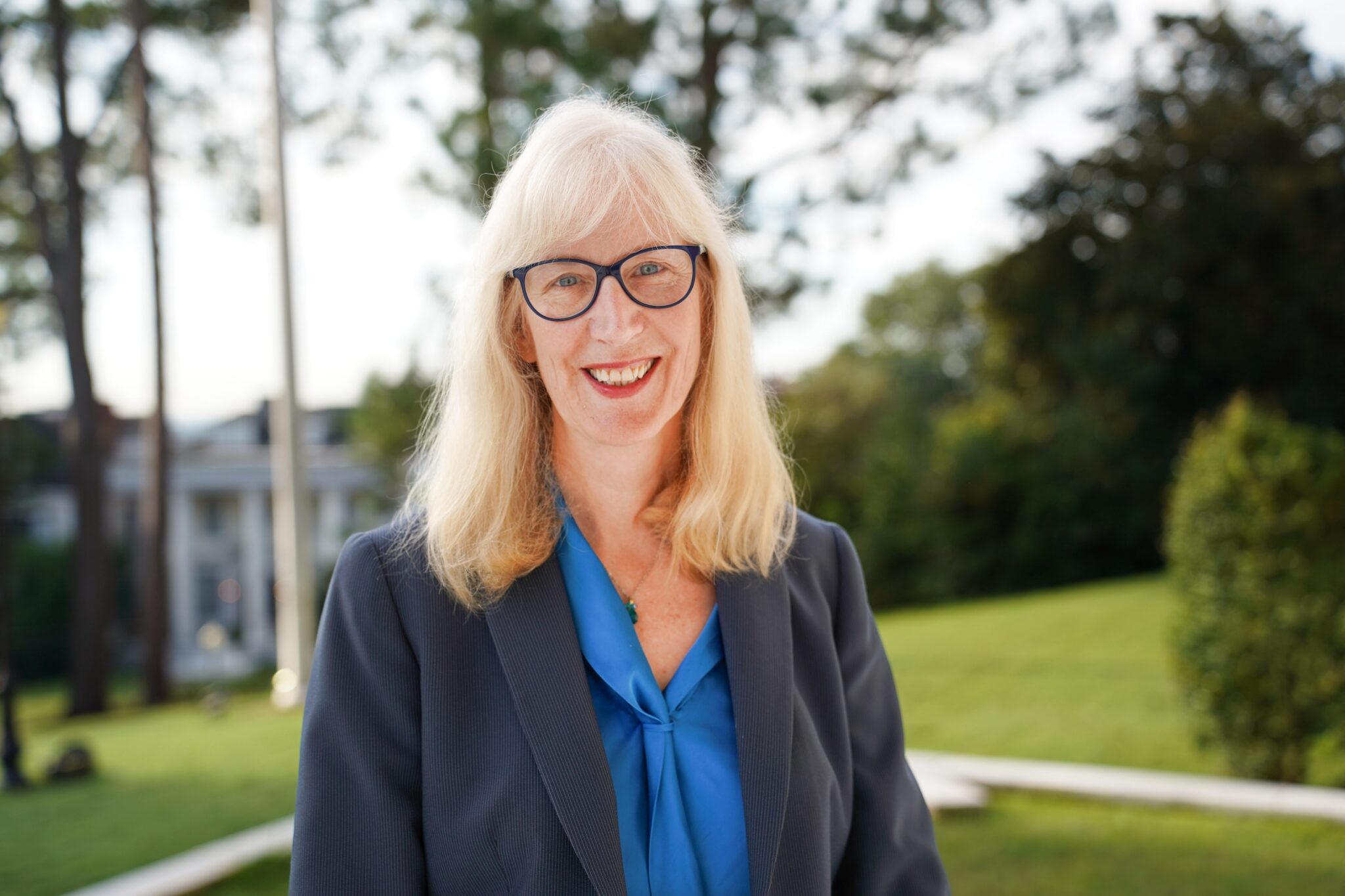 Peg McCann stands outside in a gray blazer and blue shirt