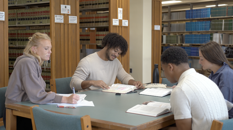 Four students reading at a table in the library