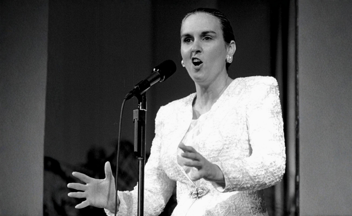 Judge Vi Bennett stands in a white dress in front of a microphone